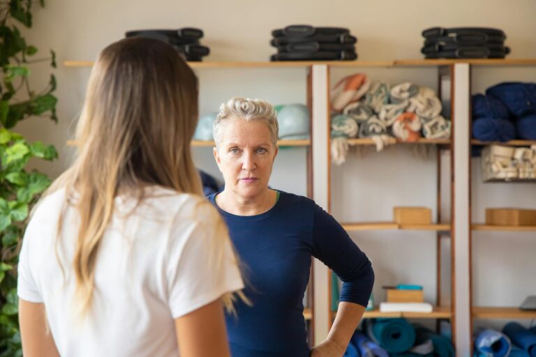 An instructor confidently engages with a student in a yoga studio setting, surrounded by equipment.