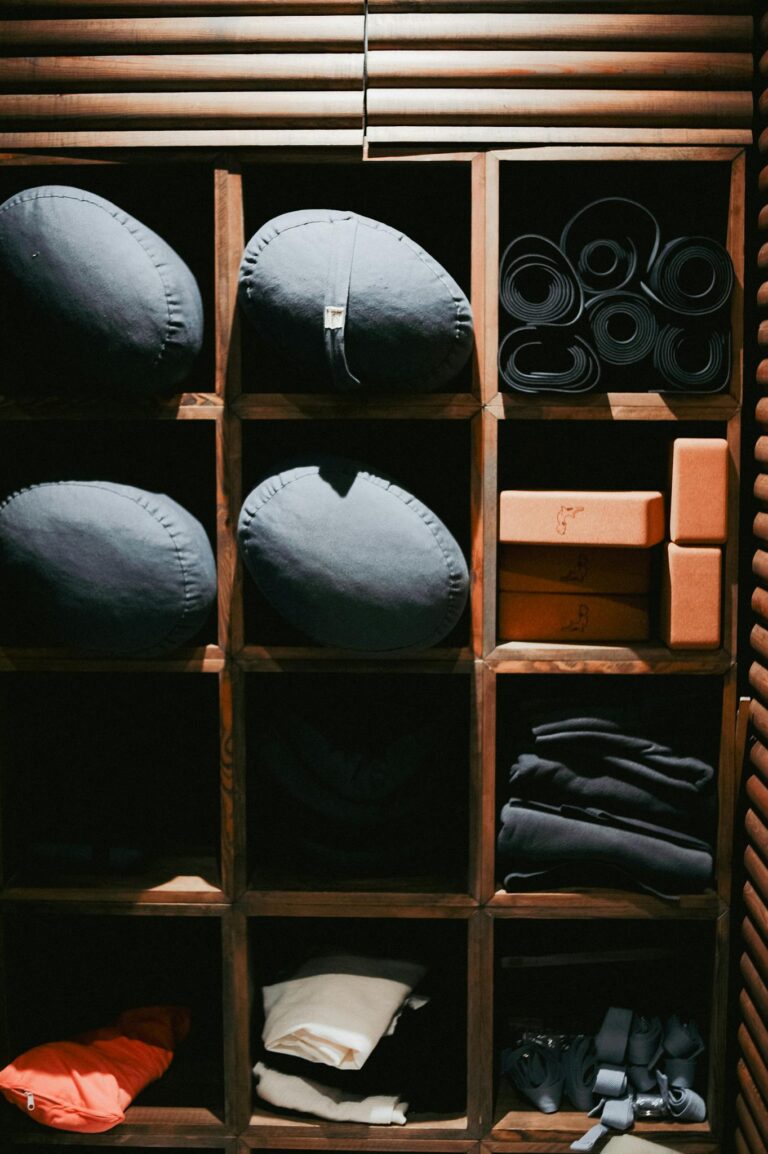Neatly arranged yoga mats, bolsters, and blocks on rustic wooden shelves in indoor setting.